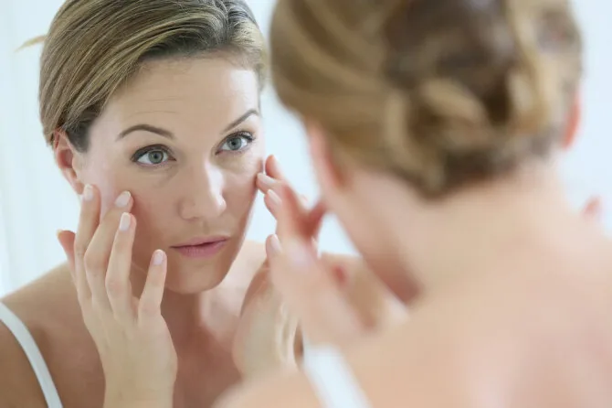 Shutterstock nuotr./Moteris tyrinėja savo veidą veidrodyje